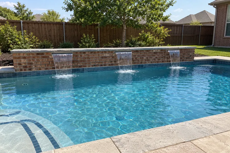 Three sheer-descent waterfalls pouring from a raised brick wall into a pool