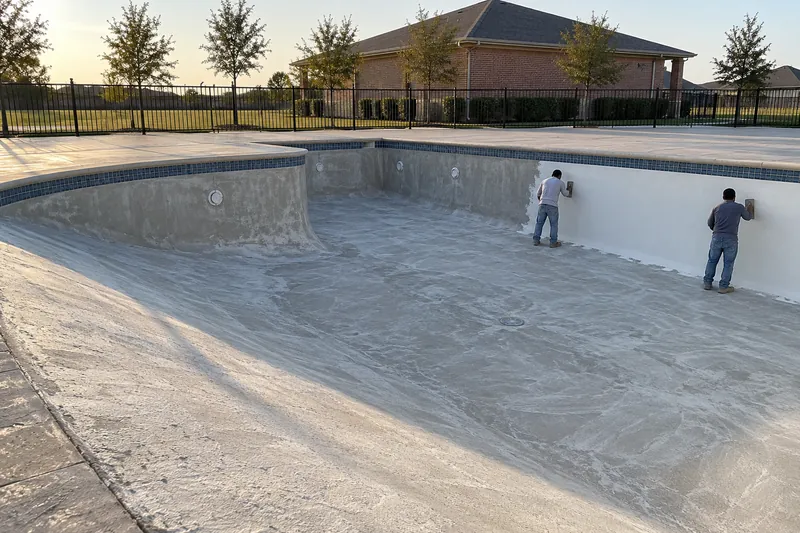 Finishers applying a white finish in a large drained community pool