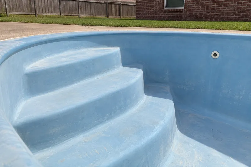 Faded, chalky gelcoat on the steps of a drained fiberglass pool