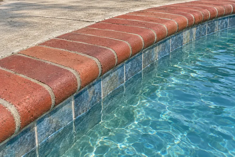 Red brick bullnose coping along the curved edge of a pool